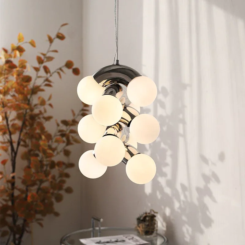 VINE Glass and steel pendant lamp with clustered frosted globes hanging in modern interior beside leafy plant and soft wall shadows.