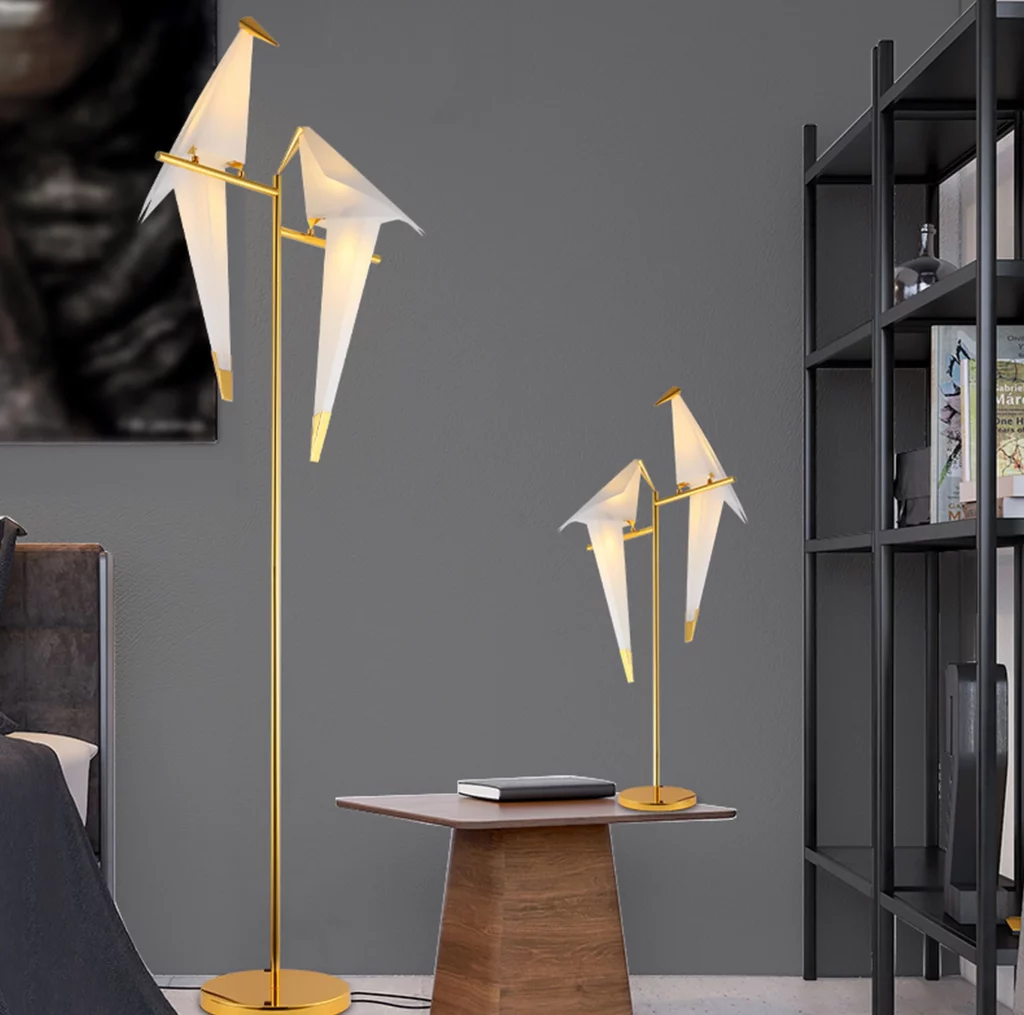 Perch Table & Floor Lamp with origami bird-shaped lights in a modern room, gold stand, side table, and shelf, warm poetic glow
