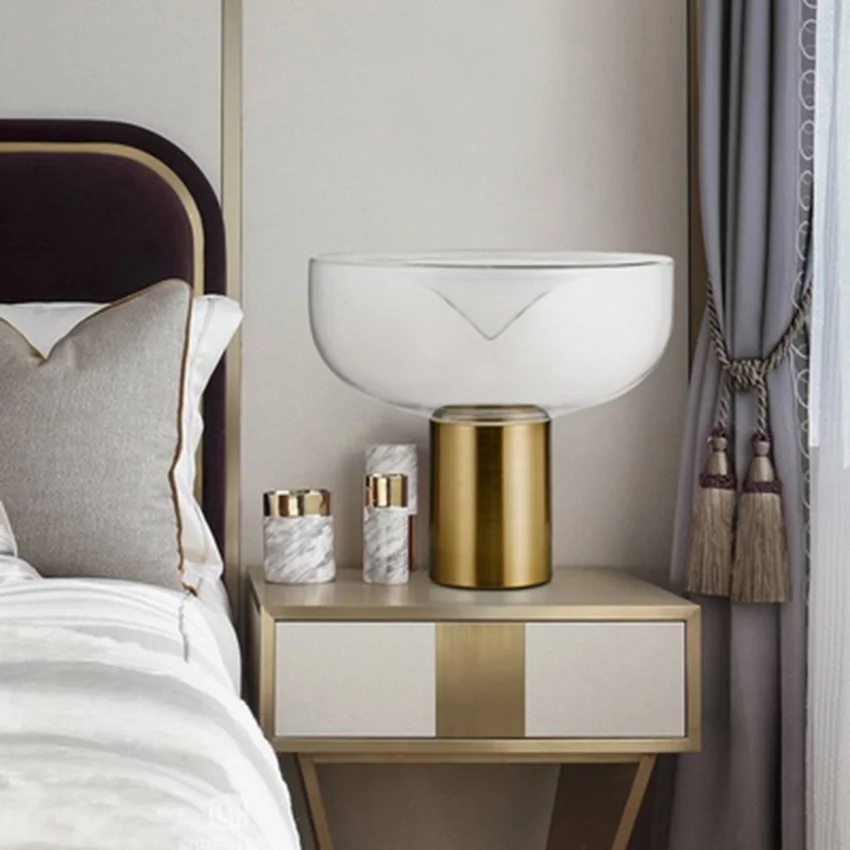 AELLA T 54 LED Blown Glass Table Lamp with a wide frosted glass shade and gold cylindrical base displayed on a modern bedside table in a stylish bedroom.