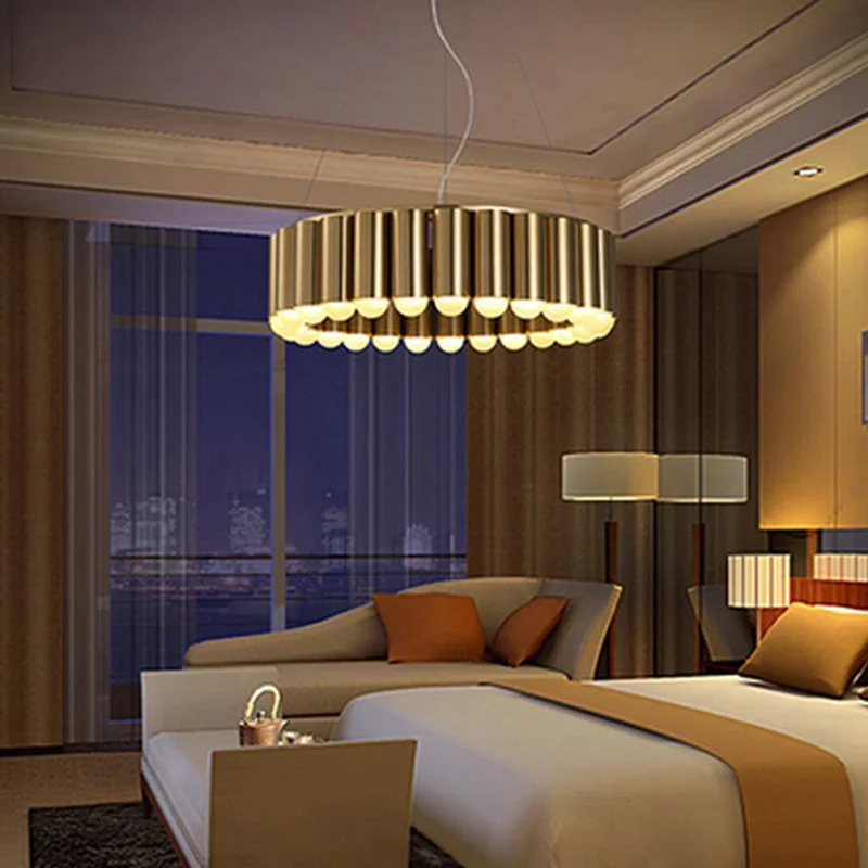 Carousel LED Chandelier with golden vertical slats glowing warmly in a luxurious bedroom at night. It hovers over beige sofa, orange pillows, bed with brown bedding, lamps, and city skyline through large window.