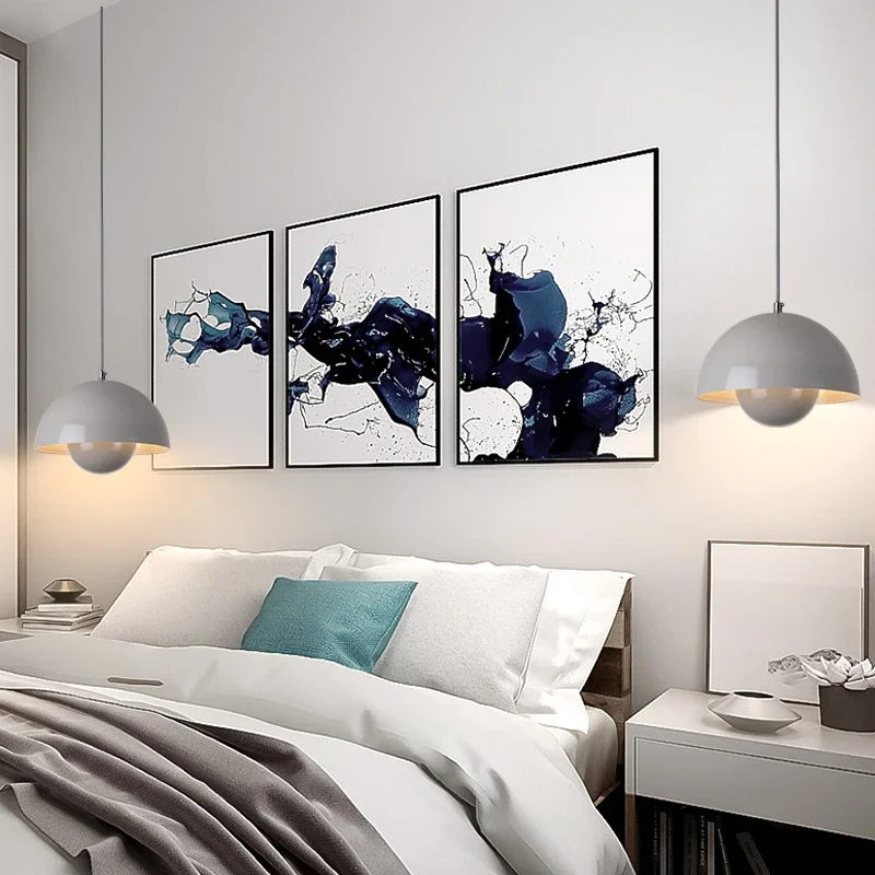 Two matte grey Flowerpot VP7 Pendant lamps hang on either side of a white bed with blue and grey accents, above white nightstands and below three abstract navy blue artworks.