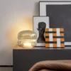 Macaron Table Lamp with a stylish, stacked glass design, placed on a sleek side table alongside abstract art and a minimalist portrait.