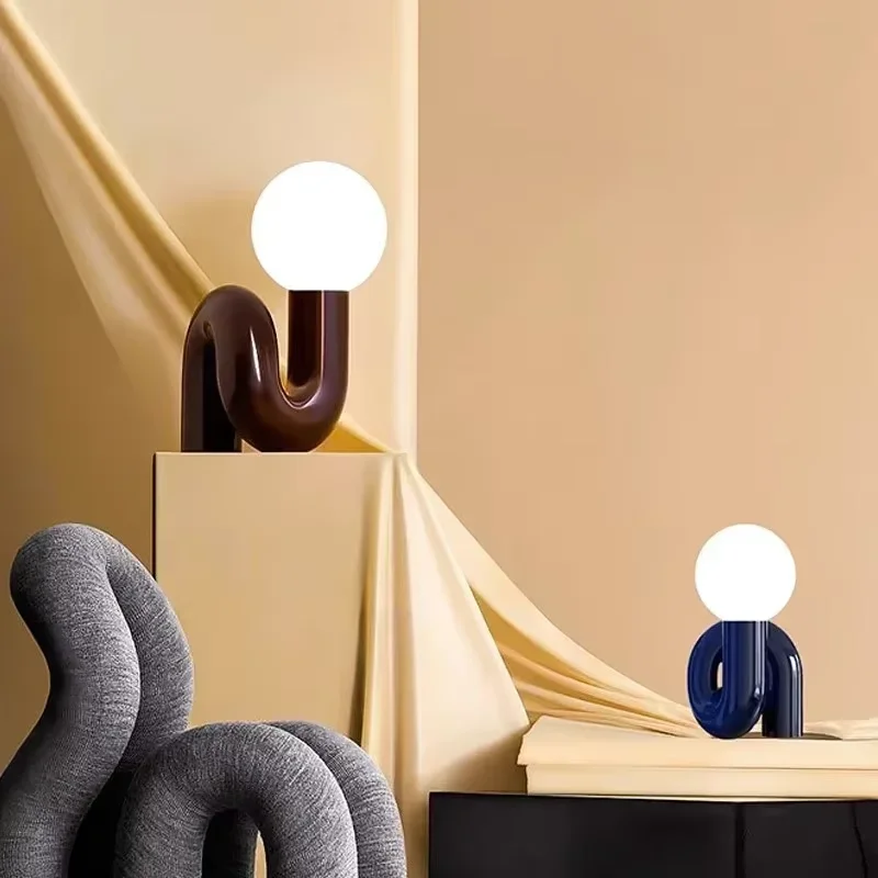 The Adalyn Table Lamp features sculptural, curved bases in brown and blue with round white globes on top, set against a soft backdrop.