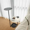 A modern Flat Floor Lamp with a sleek black design stands next to a white side table, featuring a small light and a coffee cup.