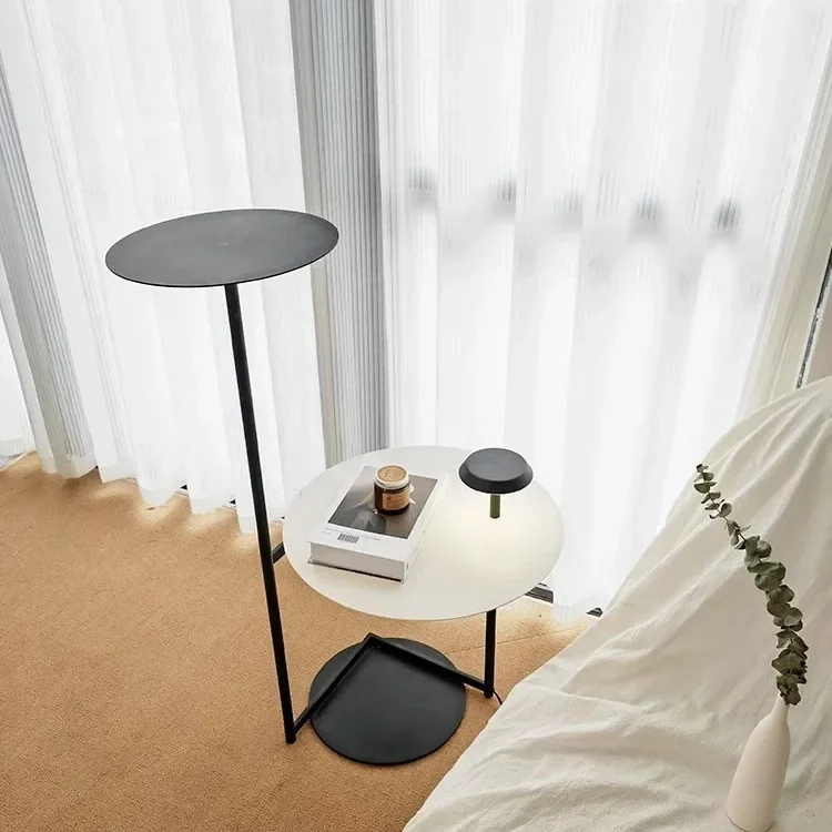 A modern Flat Floor Lamp with a sleek black design stands next to a white side table, featuring a small light and a coffee cup.