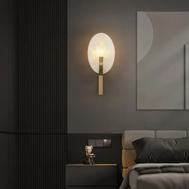 The Applique Alice Wall Lamp features an elegant oval light fixture with a brass base, complementing a modern dark bedroom setting.