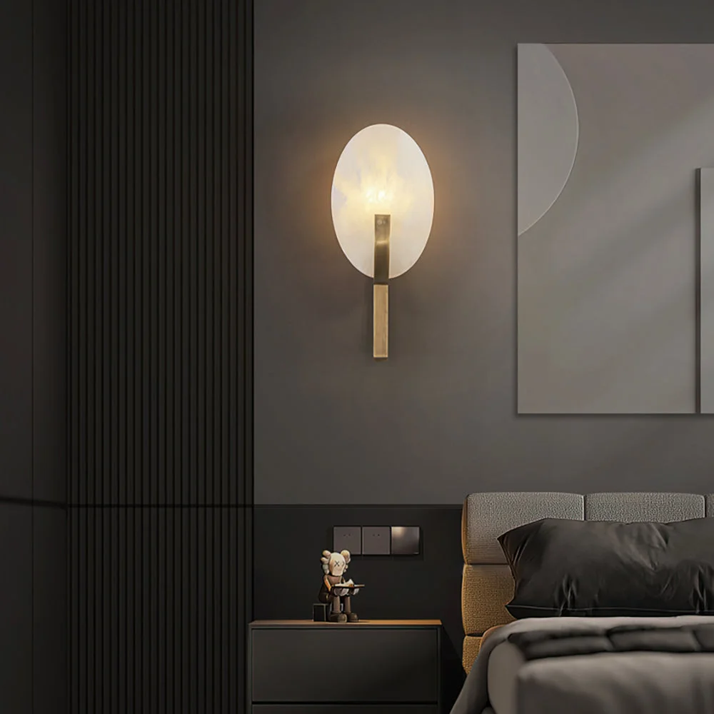 The Applique Alice Wall Lamp features an elegant oval light fixture with a brass base, complementing a modern dark bedroom setting.