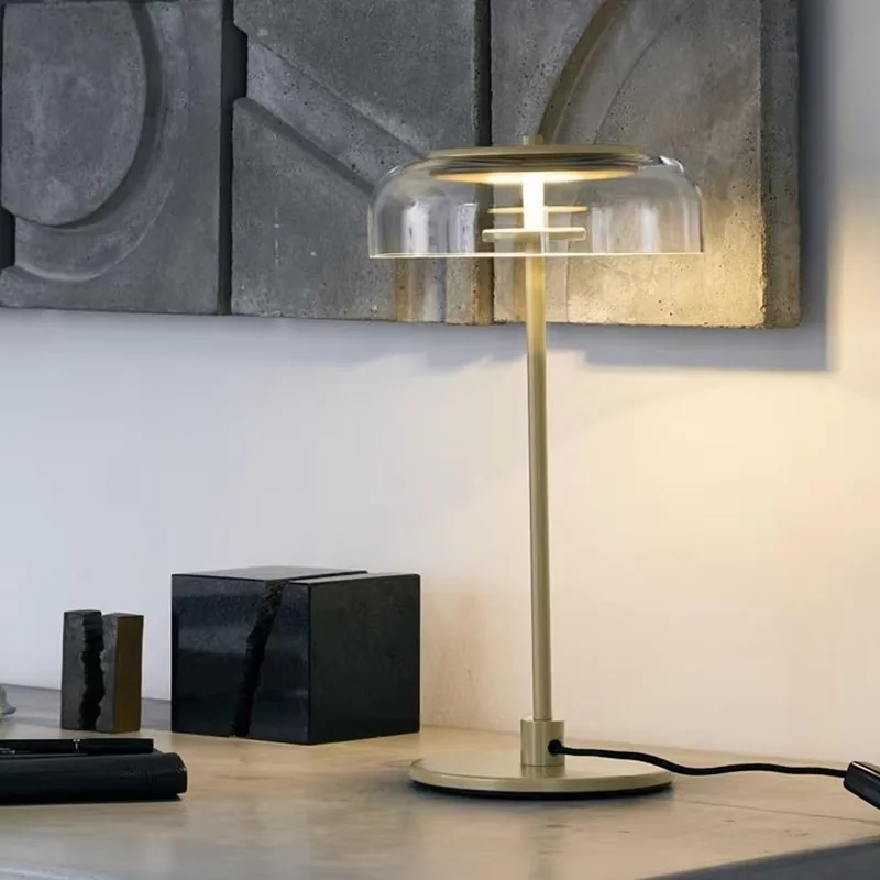 Blossi Table Lamp with a clear glass dome and a sleek, modern base, set on a minimalist desk with geometric art in the background.