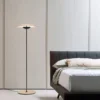 A sleek GINGER Floor Lamp stands beside a modern bed, adding soft lighting to the minimalist bedroom.