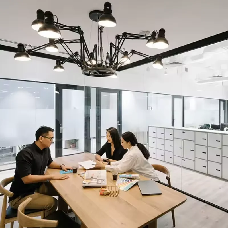 Team meeting at modern glass office table under Dear Ingo Suspension Lamp, with designers reviewing samples and documents in bright workspace.